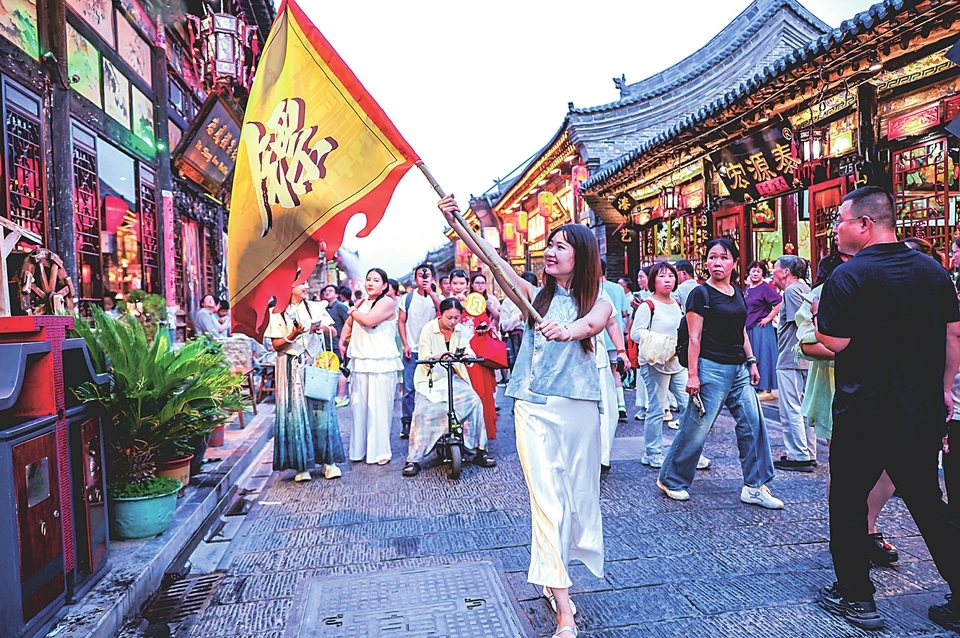 平遥古城内，游客手举镖旗互动打卡。（王昕 摄）